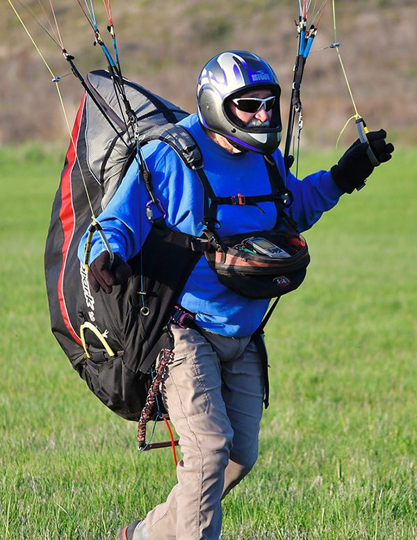 Person paragliding over grassy field, wearing helmet.
